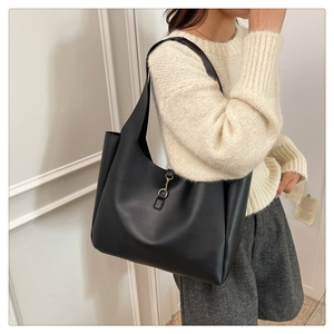 Close-up of black leather tote bag with gold metal clasp on a beige knit sweater