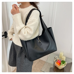 Fashionable black leather tote bag with gold clasp shown on shoulder in lifestyle setting