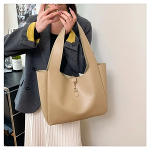 Detail of khaki leather tote bag featuring wide handles and a secure metal clasp closure