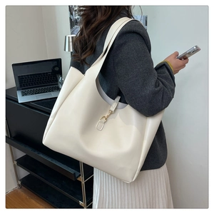 Detail view of large cream tote bag with metal clasp on shoulder in office setting