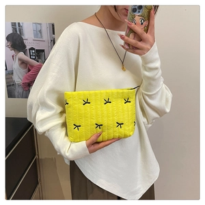 Détail d'une pochette jaune matelassée avec motifs de nœuds noirs et texture ondulée