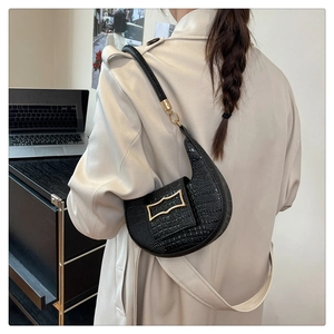 Lifestyle shot of black crocodile embossed crescent shoulder bag worn with a trench coat