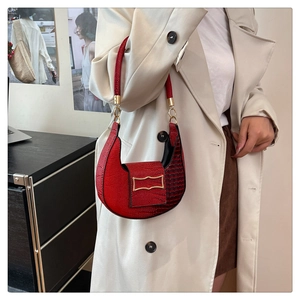 Detail view of red crocodile pattern hobo bag with gold buckle on a beige coat model