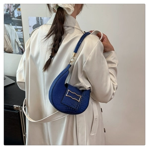 Detail of dark blue hobo bag with crocodile texture and gold wavy metal buckle on model