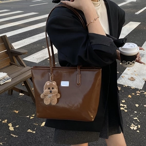 Brown patent leather tote bag with silver plaque and bear charm shown in urban street setting