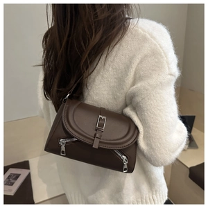Detail of dark brown leather crossbody bag with dual zippers and flap closure on a model