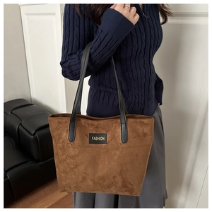 Detail of brown faux suede tote bag featuring a black fashion label and shoulder straps