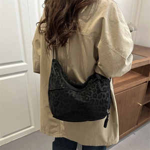 Black leopard print dumpling bag shown on shoulder in a stylish interior setting