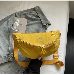 Detail shot of bright yellow nylon half-moon bag with circular metal logo and triangle zipper