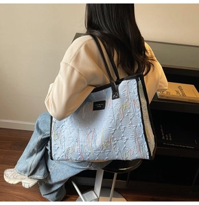 Detail of light blue quilted tote bag with wavy embroidery and black leather straps