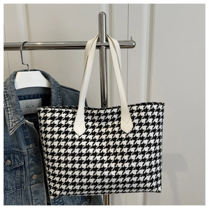 Detail of black and white houndstooth woven tote bag with white leather straps and textures