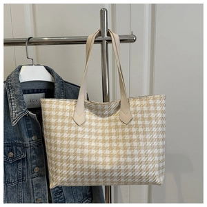Detail shot of houndstooth tote bag texture with beige handles on a garment rack