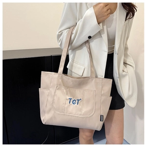 Gros plan d'un sac cabas beige avec broderie TGT bleue et étiquette latérale de mode