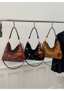Detailed view of three suede shoulder bags in brown, black and beige with silver eyelets