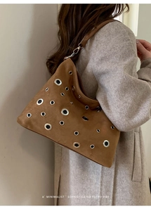 Detail of a brown suede shoulder bag with silver metal eyelets on grey coat background