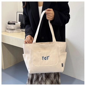 Détail du sac cabas en toile blanc cassé avec broderie TGT bleue et étiquette latérale