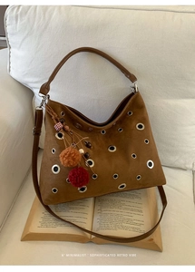 Detail view of caramel suede tote bag with metal eyelets and decorative fuzzy charm