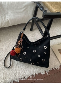 Detail of retro black hobo bag with silver eyelets and colorful bohemian tassel charm
