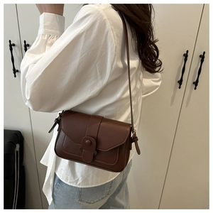 Detail of dark brown leather crossbody bag with vintage round buckle on shoulder strap