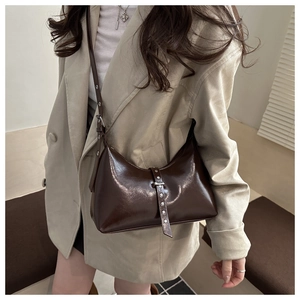 Detail of dark brown glossy hobo bag with silver eyelets on adjustable shoulder strap