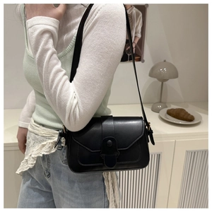 Detail of matte black leather crossbody bag featuring a wide decorative buckle and flap closure