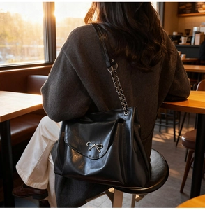 Detail of a black leather tote bag with a silver bow clasp and chain strap in natural light