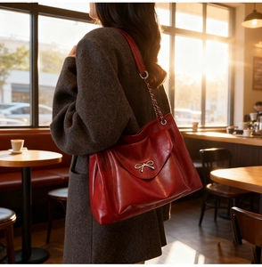 Detail of red leather tote bag with silver bow accent and chain strap in cafe setting