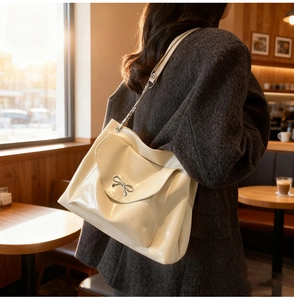Detail of cream glossy leather tote bag featuring a silver bow buckle and chain strap