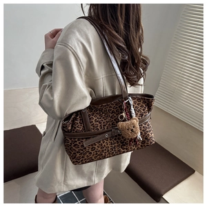 Detail of leopard print tote bag featuring brown leather straps and a plush bear charm