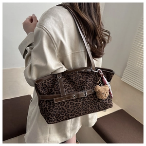Detail of leopard print tote bag with brown leather straps and plush bear charm