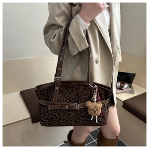 Detail of leopard print tote bag with brown leather strap and plush bear charm
