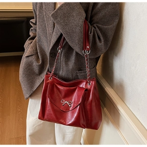 Detail of dark red shoulder bag with silver bow accent on tweed blazer model