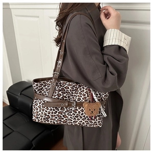 Detail of leopard print tote bag featuring brown leather strap and plush bear charm accessory