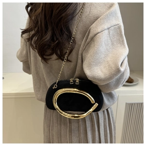 Detail of a black crossbody bag with large gold metal handle and chain strap on model