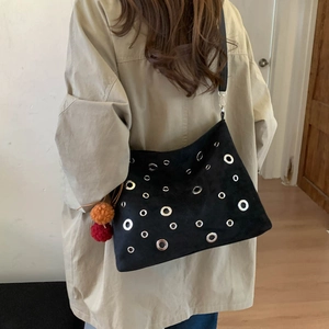 Suede biker shoulder bag with silver eyelets and colorful pom-poms on a female model