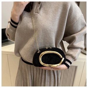 Close-up of a mini black suede clutch bag with a large golden metal handle and chain strap