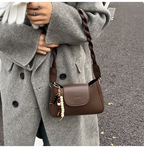 Detail of brown matte leather crescent bag featuring woven strap and beaded charm accent