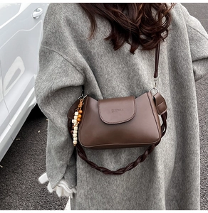 Detail of dark brown leather crescent bag featuring woven strap and wooden bead charm