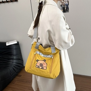 Yellow canvas tote bag with cartoon pattern and side zippers carried by model in trench coat