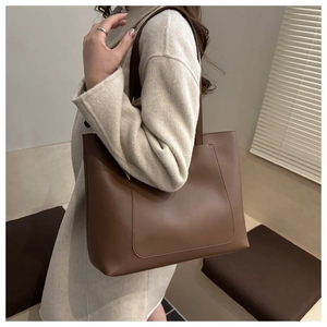 Détail du grand sac cabas en cuir marron foncé avec poche frontale porté à l'épaule