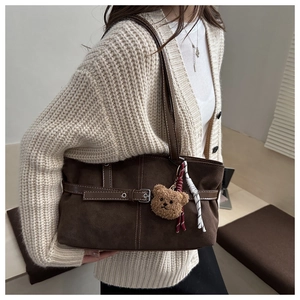 Close-up of brown faux suede shoulder bag with metal buckle strap and plush bear charm