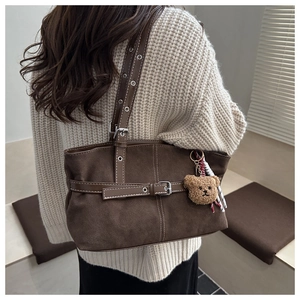 Detailed shot of dark brown suede tote bag with leather straps and a plush bear charm
