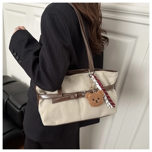 Detail of off-white canvas tote bag with brown leather trim and plush bear charm
