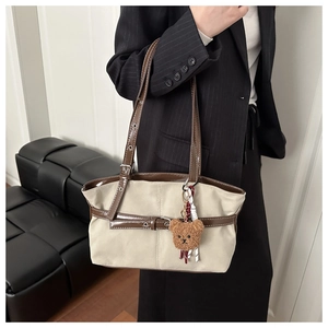Detail view of suede shoulder bag with leather trim and cute teddy bear charm on model