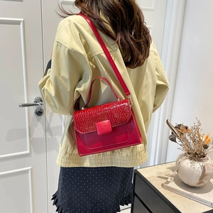Red crocodile embossed square handbag shown on shoulder in a minimalist indoor setting