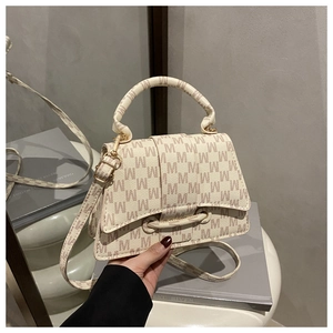 Detail view of cream textured leather handbag with brown M pattern and gold hardware