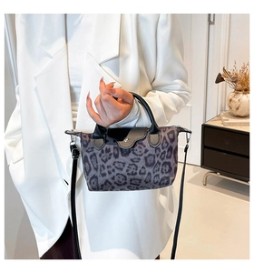 Detail of leopard print nylon handbag with black leather flap held by model in white suit