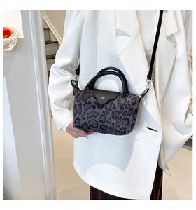 Detail of leopard print nylon handbag with black leather handle worn over a white blazer