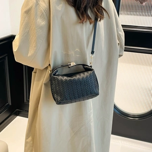 Elegant black woven leather shoulder bag with metallic clasp worn by a model in a beige coat