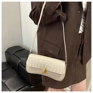 Détail du sac baguette crème avec texture croco et fermoir rotatif doré élégant